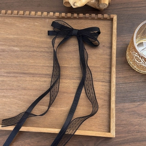 Detail of black lace bow hair clip with ribbons on a wooden tray with elegant textures