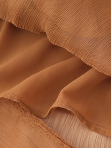 Détail macro du tissu plissé caramel montrant les textures superposées et les coutures fines