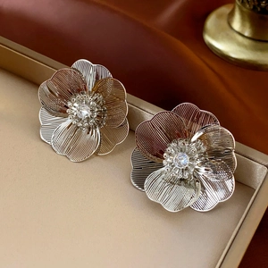 Macro shot of silver flower earrings with brushed metal petals and zircon center stone