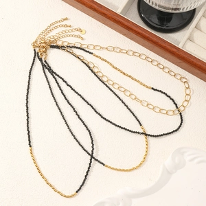 Layered black spinel beaded necklace and gold link chain set on textured surface