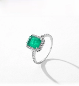 Macro detail of emerald-cut green gemstone ring with halo diamond setting and silver band