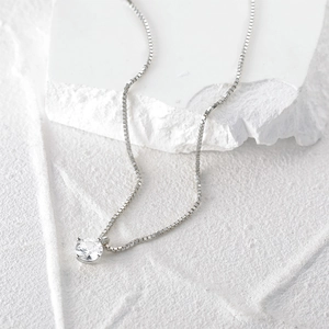 Macro detail of a single round zircon pendant on a silver box chain over white stone