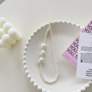 Detail of beaded phone strap with white pearls and iridescent heart charms on a plate
