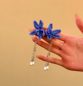 Close-up of blue beaded flower earrings with silver chains and pearl drops detail