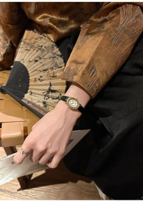 Detail of an oval gold watch with diamond-set bezel and retro black leather strap