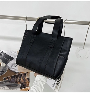 Close-up of black PU leather tote bag hanging on metal stand with lifestyle props