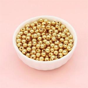 Golden beads for DIY jewelry making in a white bowl over a soft pink background