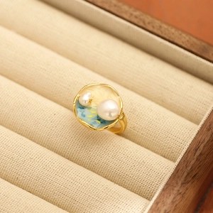 Détail d'une bague vintage en émail avec perles et métal doré dans un écrin à bijoux