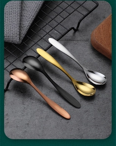 Polished stainless steel spoons in rose gold, black, gold and silver on a rustic stone background