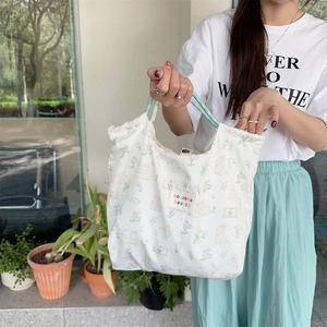 Close-up of a white canvas tote bag with bunny patterns and green braided handles