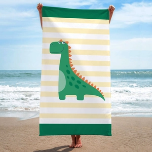 Green cartoon dinosaur beach towel held by hands against a sunny ocean background