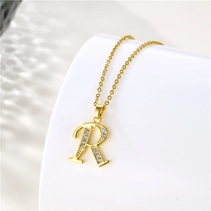 Macro shot of 18K gold letter R pendant necklace with sparkling clear zircon crystals