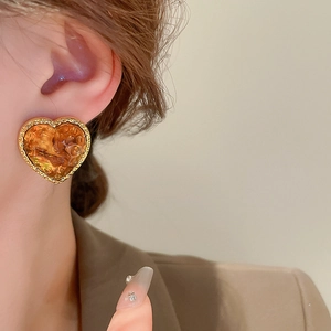 Close-up of heart-shaped amber resin earrings with vintage gold-plated textured edges