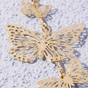 Macro shot of long hollow gold butterfly earrings showing detailed metallic texture