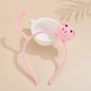 Pink hand-knit headband featuring cute pig character with ceramic cup and soft shadows