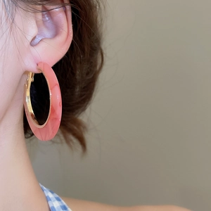 Close-up of a pink resin C-shaped hoop earring with gold base on a model's ear