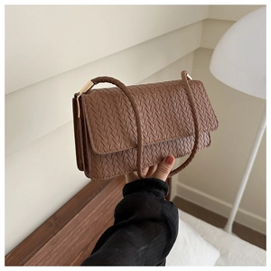 Detail of brown woven faux leather shoulder bag featuring metal clasp and textured finish