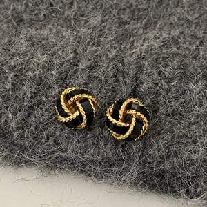 Detail of vintage gold and black enamel knot earrings on a grey felt background