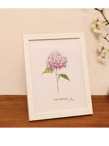 Close-up of a white wooden frame with purple hydrangea art print on a wooden desk
