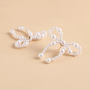 Detailed view of handmade pearl bow earrings with golden metal studs on a beige background