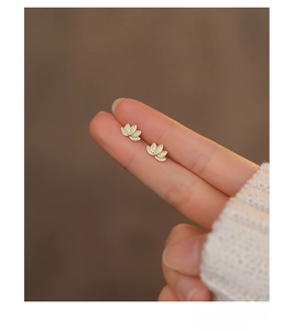 Detailed close-up of golden S999 sterling silver lotus stud earrings held on a finger