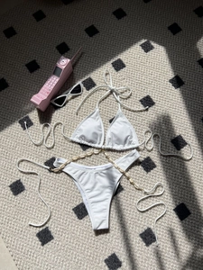 White halter bikini set with shell chain charms on geometric patterned background