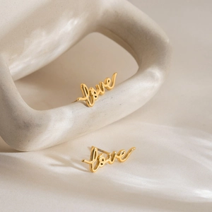 Minimalist 18K gold plated stainless steel LOVE letter stud earrings on white ceramic base
