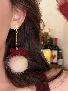 Detail of Christmas earrings featuring golden snowflake, red bow, and white fuzzy pompom