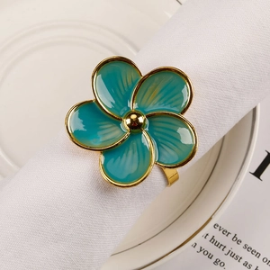 Detailed close-up of teal enamel flower napkin ring with gold plating on a white napkin