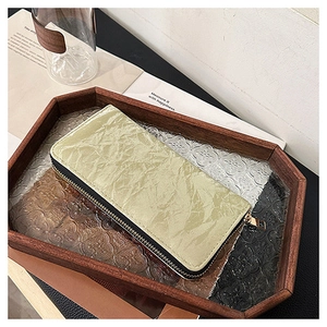 Detail view of long sage green wrinkled wallet with golden zipper in a wooden tray
