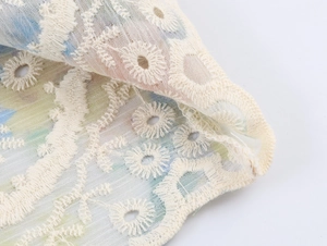 Detailed macro view of beige floral embroidery on translucent mesh fabric with rolled hem
