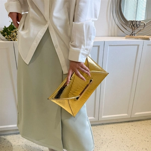 Golden crocodile embossed envelope clutch bag shown in a stylish lifestyle setting