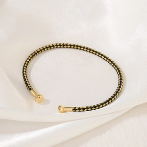 Detail of hand-woven black and gold cord bracelet with polished spherical metal ends