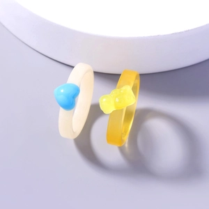 Close-up of resin heart ring and gummy bear ring on purple and white background