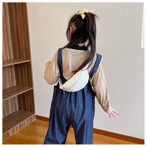 Rear view of a child wearing a white quilted crossbody bag in a modern room setting