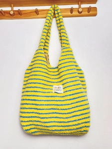 Close-up of yellow and blue striped plush tote bag hanging on a wooden hook.