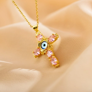Macro shot of gold cross pendant with pink faceted stones and evil eye bead