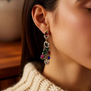 Close-up of vintage gold earrings with colorful rhinestones on a model wearing beige knit