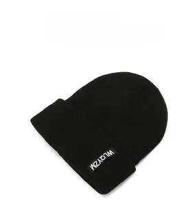 Detail of black ribbed knit beanie featuring a minimalist white lettered fabric label