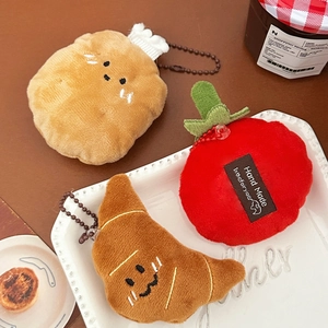 Detailed close-up of plush croissant and tomato charms on a rustic wooden table setup