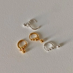 Detail of beaded hoop earrings in gold and silver finish with spherical charms