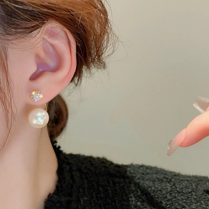 Close-up of gold-plated zircon stud earrings with a white pearl pendant on a model's ear