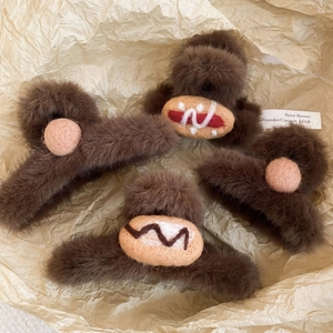 Detail of four brown acrylic hair claws with pink felt accents on a warm paper background