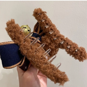 Brown plush hair claw clip with dark blue ribbon bow and festive gold bell detail