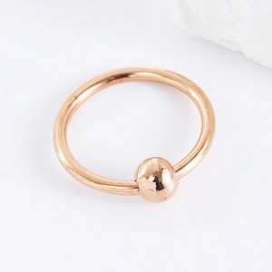 Macro shot of rose gold stainless steel piercing ring with ball closure on white background