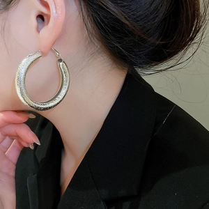 Detail view of large silver hoop earrings with fine frosted glitter texture on model