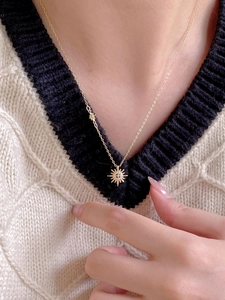 Model wearing a 18K gold starburst pendant necklace with zircon on a knit sweater