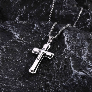 Macro shot of silver layered cross pendant with bead chain on black textured mineral stone