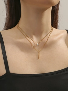 Gros plan d'un collier double épaisseur en titane doré avec cristal goutte et pendentif barre