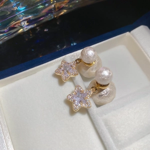 Macro detail of gold-plated star pearl earrings with cubic zirconia on white velvet